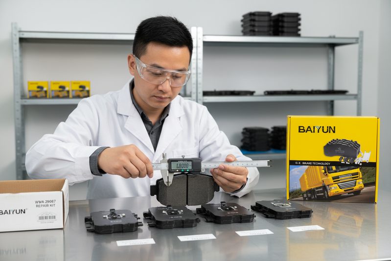 BAIYUN Brake technician inspecting commercial vehicle brake pad friction material and edge codes in quality control lab.