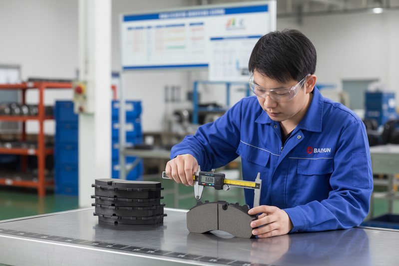 BAIYUN Brake factory technician inspecting a batch of quiet ceramic brake pads on a production line in an IATF 16949 certified facility.